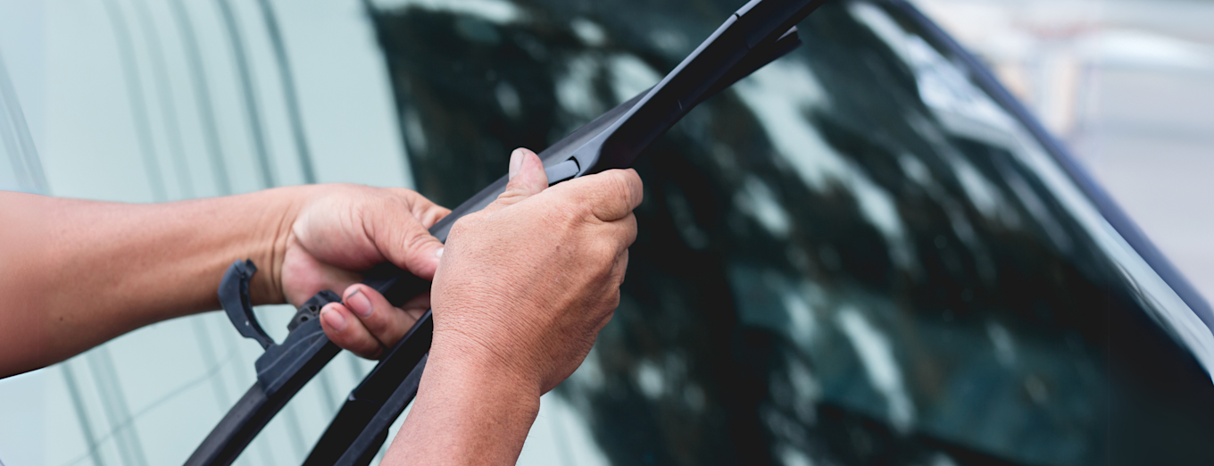 Nærbilde av hender som bytter vindusvisker på bil.
