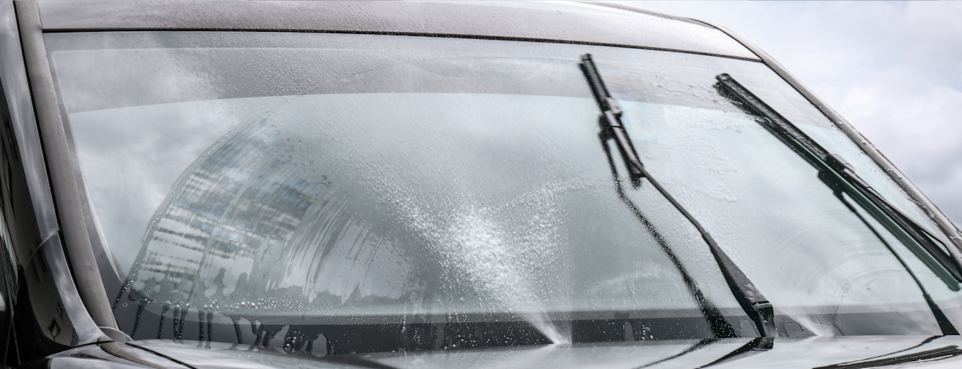 Vindusviskere i bevegelse som rengjør en våt frontrute på bil.