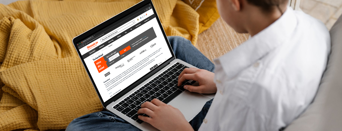 Person sitter i sofa med gult pledd og bruker en bærbar PC for å besøke Skruvat.no.
