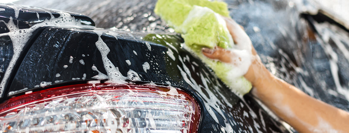 Håndvask av svart bil med skum og svamp.