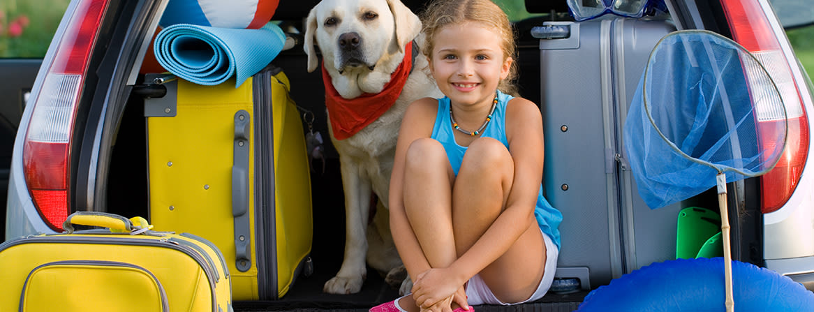 Jente og hund i bilens bagasjerom omgitt av kofferter.