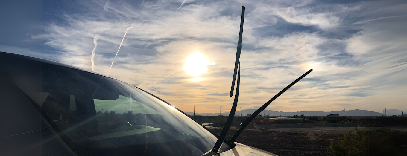 Bil med vindusviskere oppfelt i sollys ved landevei.