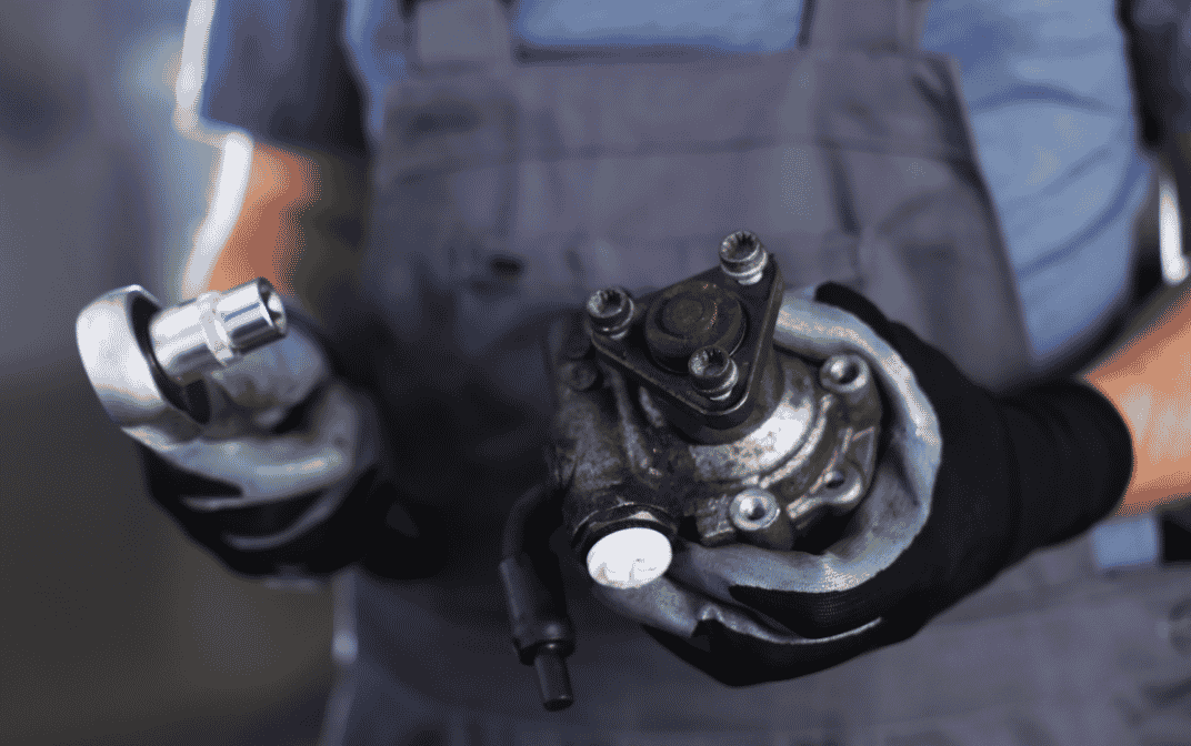 Nærbilde av en mekaniker som bruker en skralle til å jobbe på en bildel med synlige bolter.