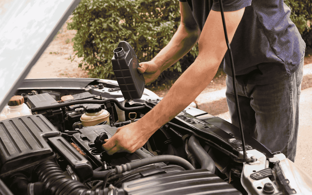 Person fyller på motorolje i bilens motor med åpent panser