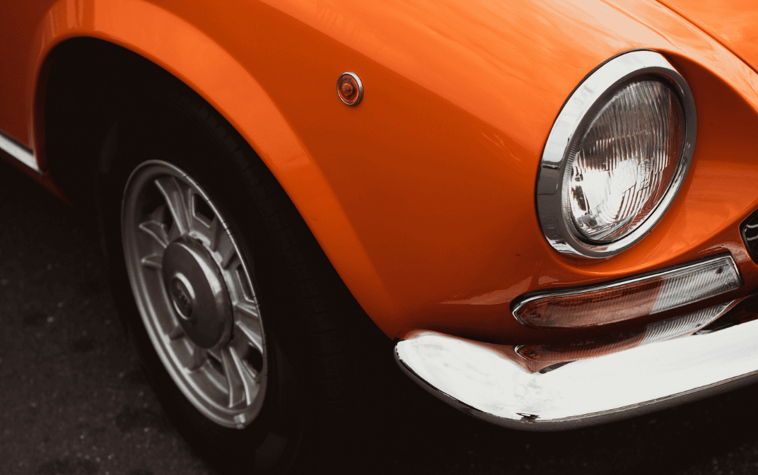 Nærbilde av en oransje bil med frontlykt og forhjul.