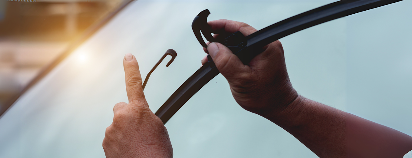 Nærbilde av hender som monterer vindusvisker på bil i solskinn.